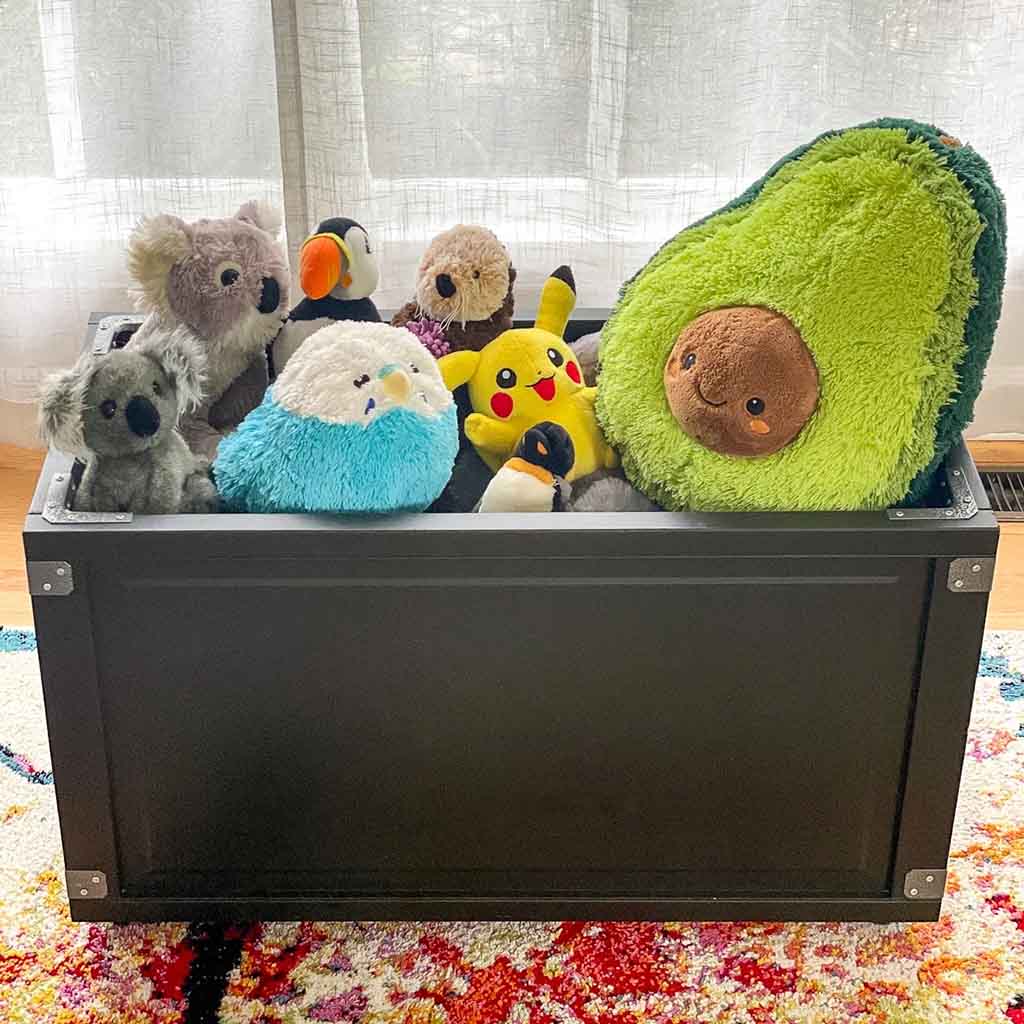 Black wooden toy chest filled with assorted plush toys and stuffed animals, offering practical living room or bedroom storage for children’s toys.