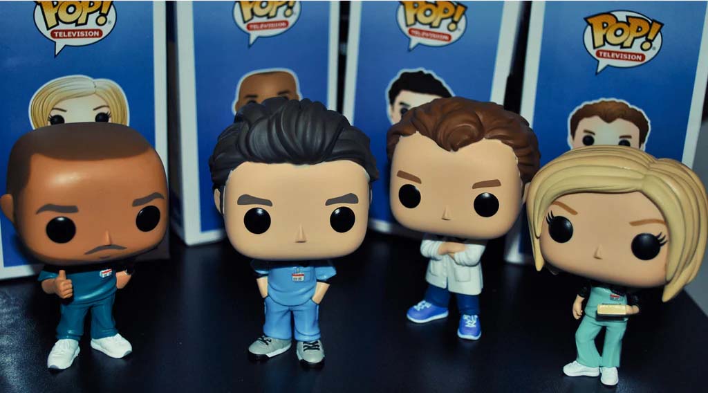 Funko Pop vinyl figures of characters from the TV show Scrubs, displayed in front of their Pop Television boxes, including stylized versions of J.D., Turk, Dr. Cox, and Elliot Reid in medical outfits.