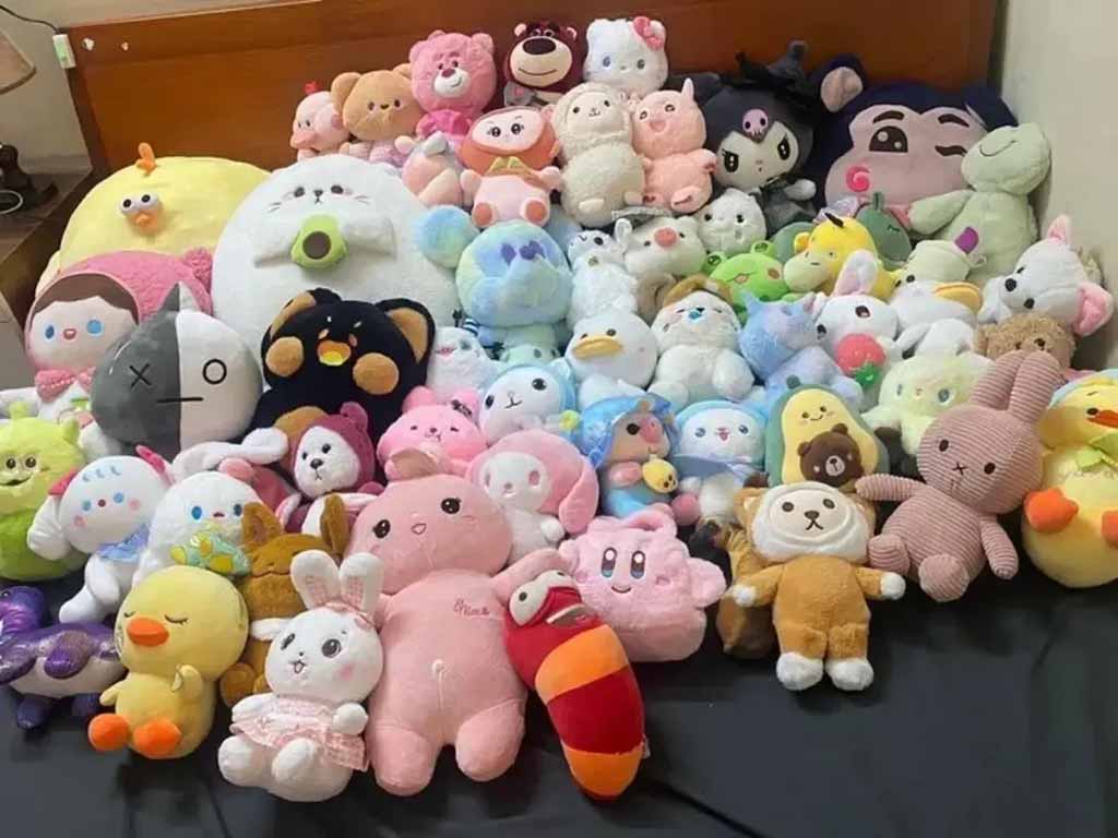 A large assortment of colorful plush toys arranged on a bed, including bunnies, bears, ducks, cartoon characters, and pastel kawaii plushies in various sizes, creating a cute and cozy display.