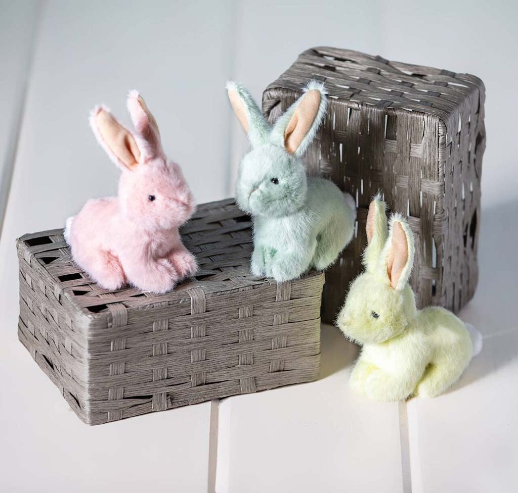 Three pastel bunny plush toys displayed on woven storage boxes.