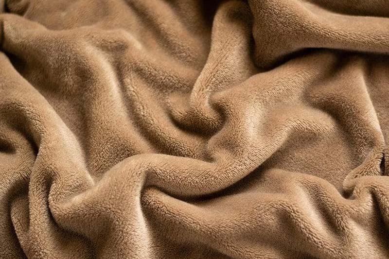 Close-up of brown plush micro-fleece fabric arranged in soft folds, highlighting a dense, velvety surface, warm tone, and smooth, cozy texture commonly used for blankets and plush toys.