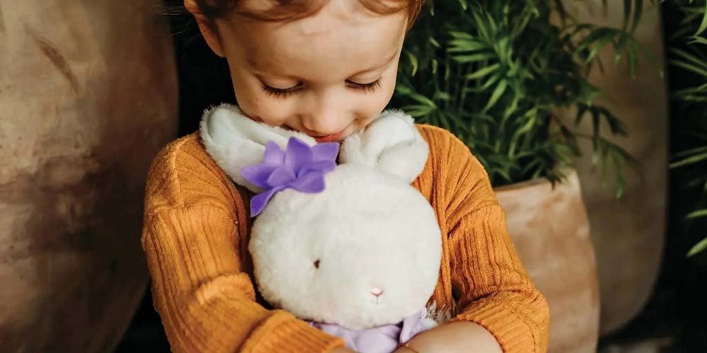 Young child gently hugging a soft white bunny plush toy with a purple bow, highlighting emotional comfort, plush toy softness, and child-friendly design, ideal for illustrating safe, high-quality stuffed animals for toddlers, gifts, and premium plush toy manufacturing inspiration.