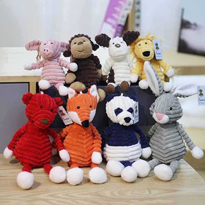 A group of soft corduroy animal plush toys, including a pig, monkey, dog, lion, bear, fox, panda, and rabbit, arranged on a table as a colorful collection of stuffed animals.