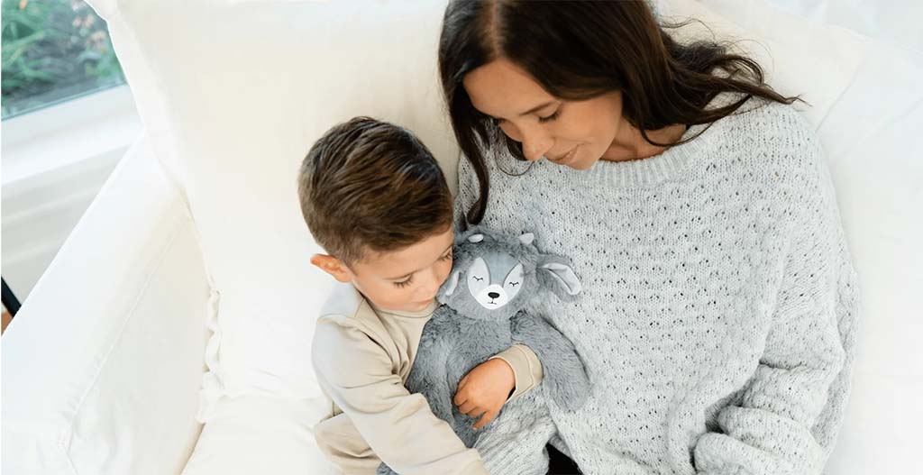 “Young child holding a soft blue plush toy while walking hand in hand with an adult, outdoors against a gray wall.”