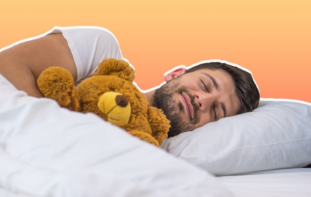 A man peacefully sleeps in bed while cuddling a soft brown teddy bear, showing how stuffed animals provide comfort and emotional support for adults.