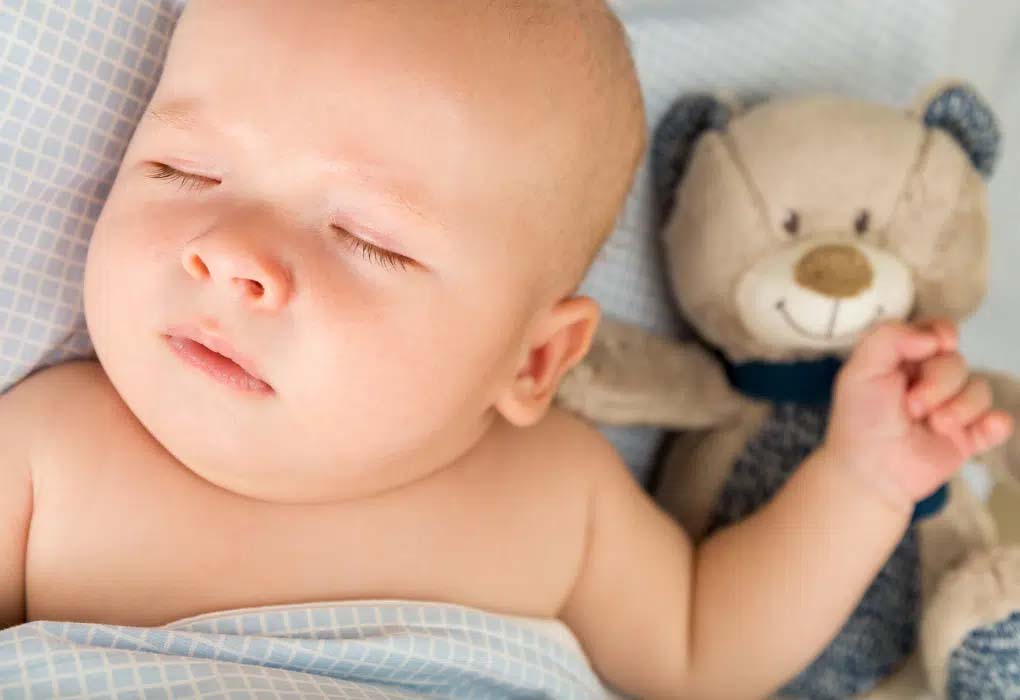 Peacefully sleeping newborn baby lying on soft bedding beside a plush teddy bear, representing comfort, security, and infant sleep environment, commonly associated with baby stuffed animals, nursery décor, and early childhood emotional bonding.