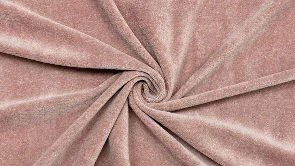 Close-up of soft blush-toned velour fabric arranged in a spiral fold, highlighting short pile texture, gentle sheen, and smooth hand feel commonly used in plush toy surfaces.