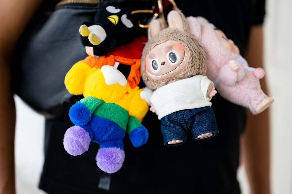 Colorful plush keychain dolls clipped to a bag, including a rainbow teddy bear and a big-eyed vinyl-face bunny character wearing casual clothes.