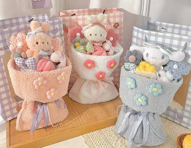 Three pastel plush toy bouquets—pink, white, and blue—each filled with soft stuffed animals, fabric flowers, and decorative ribbons, displayed with matching gift bags.