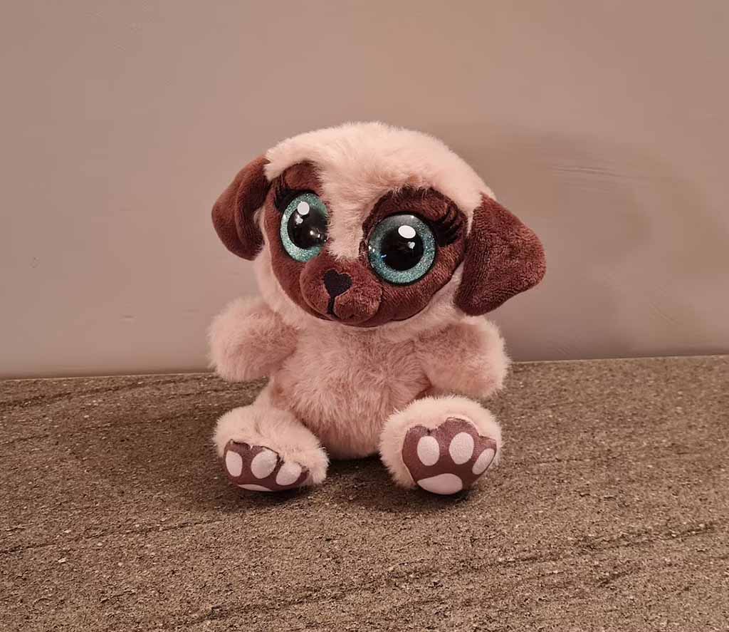Cute puppy plush toy with oversized turquoise eyes, floppy brown ears, and soft beige fur sitting on a tabletop.