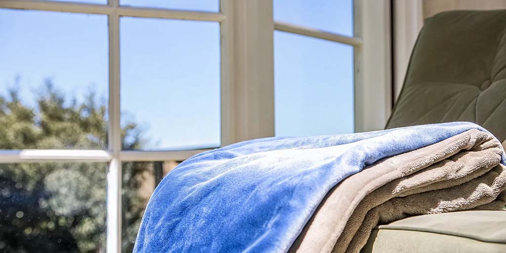 Folded plush minky blanket displayed on sofa near window, showcasing ultra-soft short-pile fabric, smooth surface texture, layered thickness, and premium finishing, suitable for OEM plush blanket manufacturing, custom color programs, gift blankets, home textile collections, and private label bedding brands.