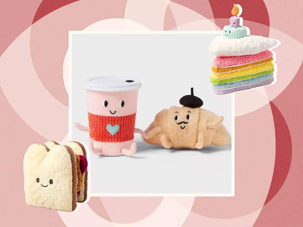Collage of adorable food-themed plush toys, including a smiling drink cup, a croissant with a beret, a rainbow cake slice with candle, and a cute sandwich plush against a pink geometric background.