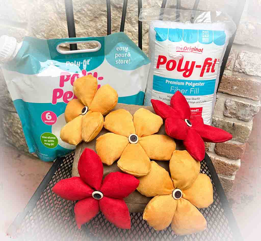 Handmade stuffed fabric flowers in yellow and red arranged on a cushion, with bags of Poly-Fil stuffing in the background.