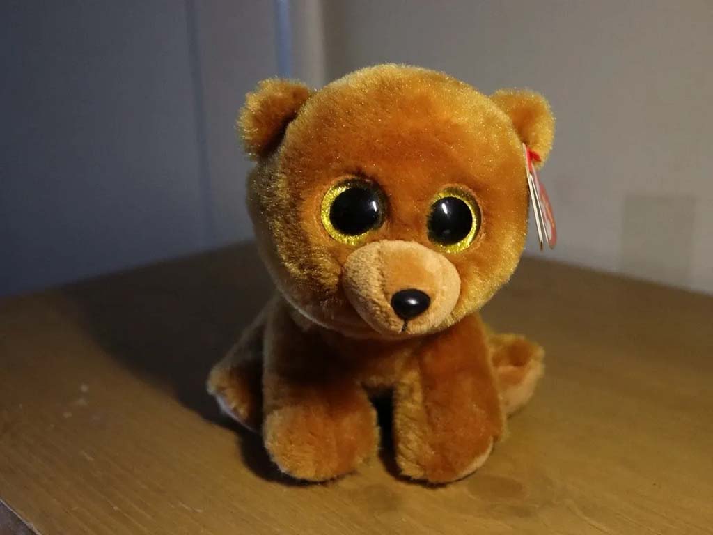 Small brown teddy bear plush toy with shiny gold eyes sitting on a wooden table