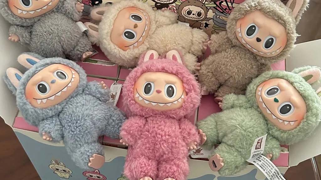 A group of fluffy Labubu plush figures in pastel colors—pink, blue, green, cream, and grey—arranged inside a themed display box. Each plush features bunny ears, soft textured fur, round expressive eyes, and the signature mischievous Labubu grin.