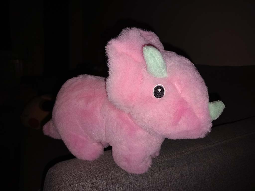 Pink plush rhinoceros toy with small horn sitting on a couch.