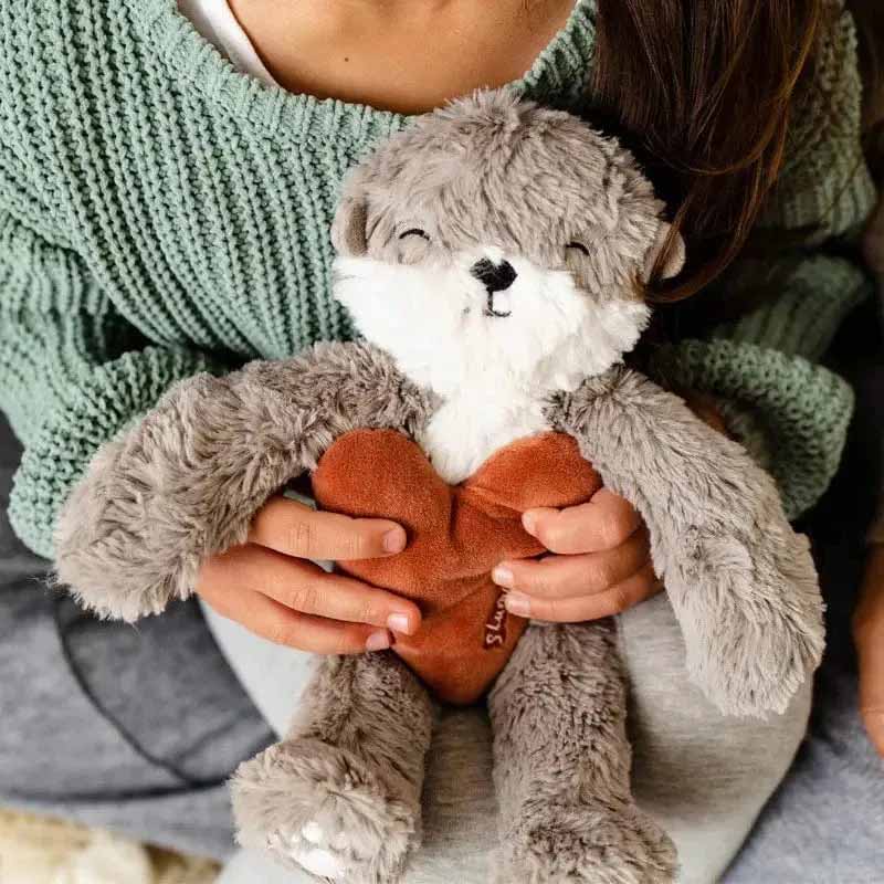 Person holding a soft gray plush otter toy with a brown heart, symbolizing comfort, affection, and emotional support through cuddly stuffed animals.