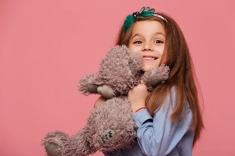 Smiling young child hugging a soft plush toy against a pastel background, showing emotional comfort, tactile softness, and child-friendly stuffed animal design made with gentle materials, secure stitching, and safe construction suitable for kids, gift markets, and everyday cuddling companionship.