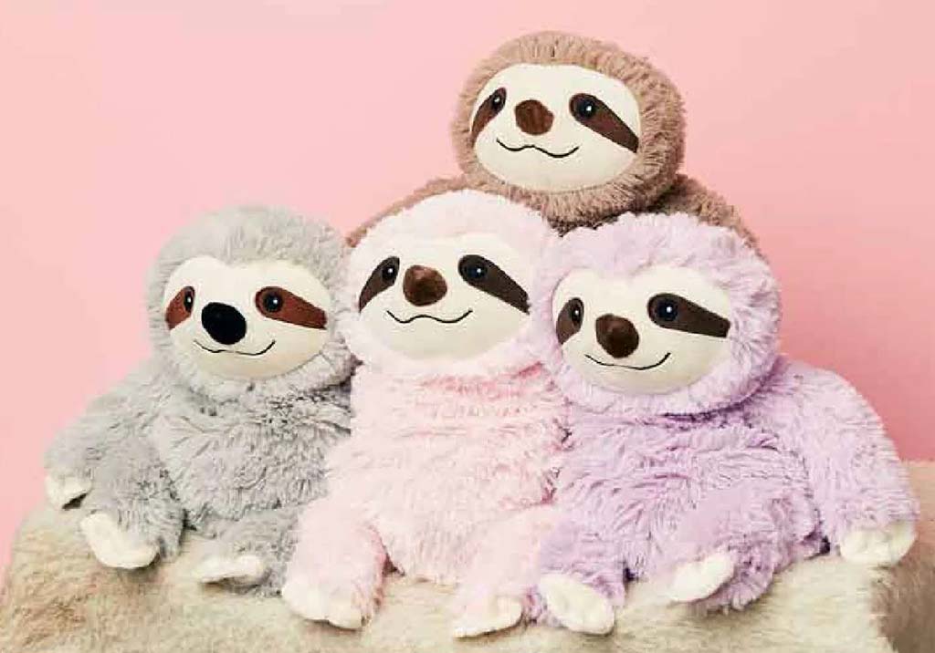 A group of four soft sloth plush toys in gray, brown, pink, and lavender sitting together against a pastel pink background, showcasing cute and cozy stuffed animals ideal for comfort and gifting.