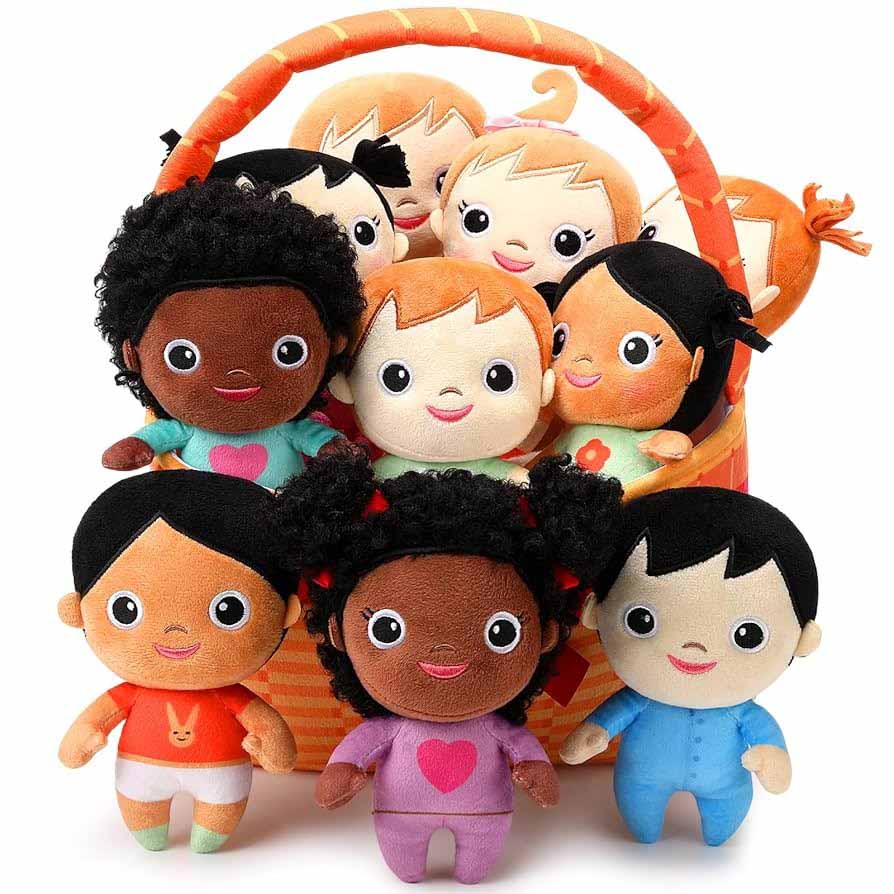 A colorful assortment of diverse plush dolls with different skin tones, hairstyles, and outfits arranged inside and in front of an orange basket, showcasing inclusive soft toy characters for children.
