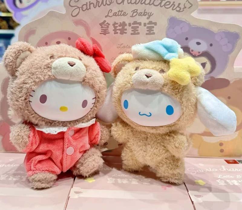 Two cute Sanrio Latte Baby plush dolls displayed side by side, featuring Hello Kitty in a pink bear suit with a red bow and Cinnamoroll in a beige bear suit with pastel star accessories, set against a themed background.