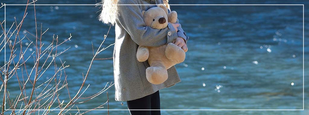 Child holding a teddy bear near a river outdoors, showing emotional attachment to a plush toy, comforting stuffed animal use, and lifestyle imagery commonly used in plush toy branding, storytelling, and consumer marketing visuals.