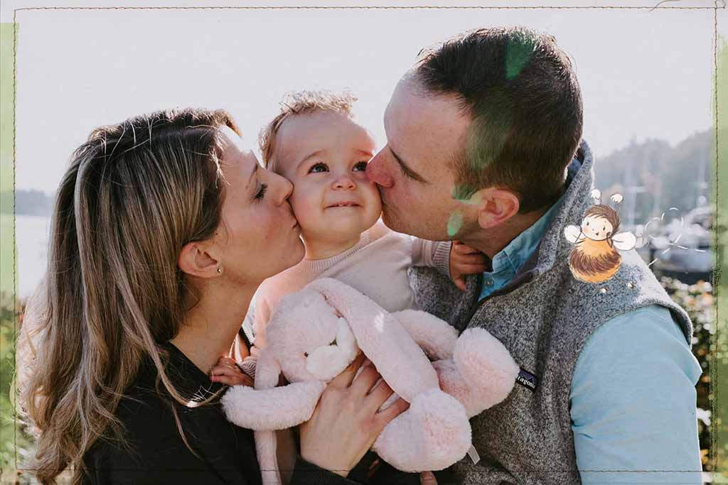 Parents kissing their baby while holding a soft bunny plush toy.