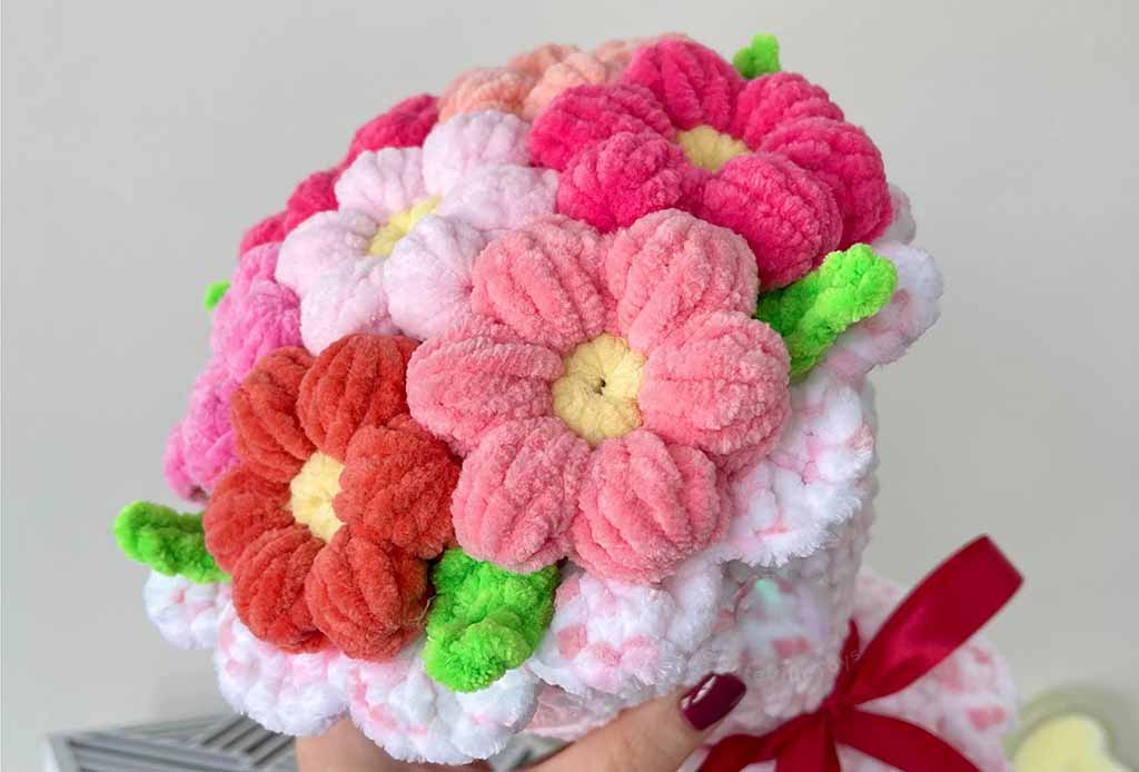 A handmade bouquet of soft plush flowers in pink, red, and white tones with green leaves, held together with a ribbon.