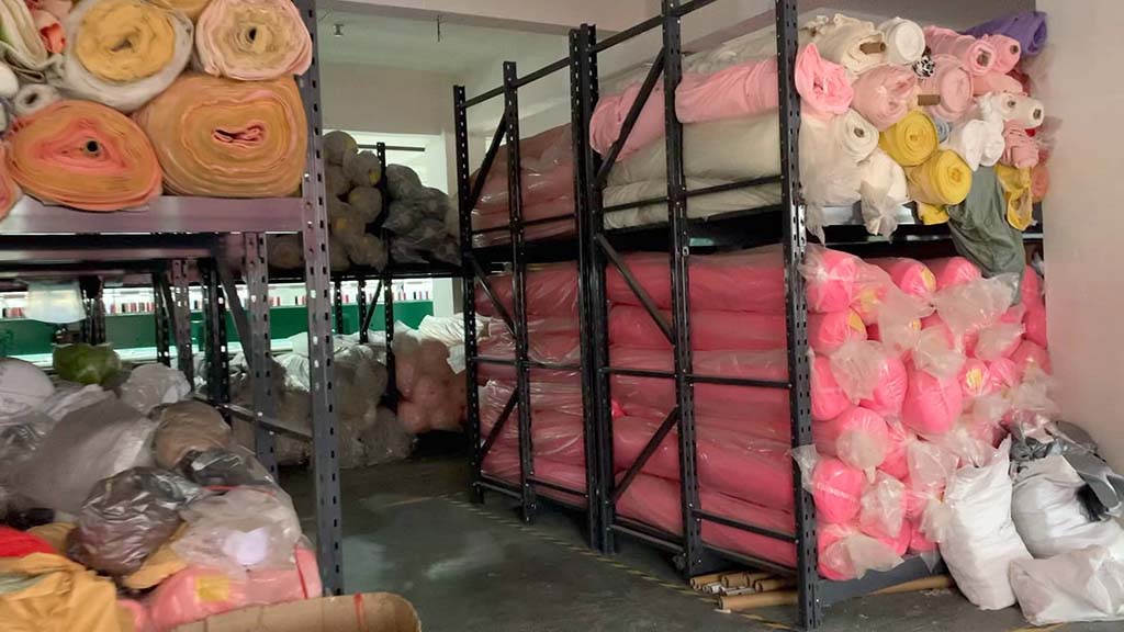 Shelves filled with colorful rolls of plush fabric stored in a warehouse for toy manufacturing.