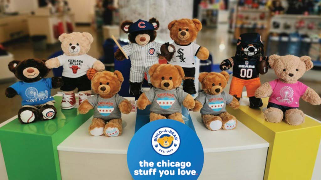 A display of Build-A-Bear teddy bears dressed in Chicago sports team outfits, including baseball, basketball, and football uniforms, arranged on colorful platforms inside a retail store.