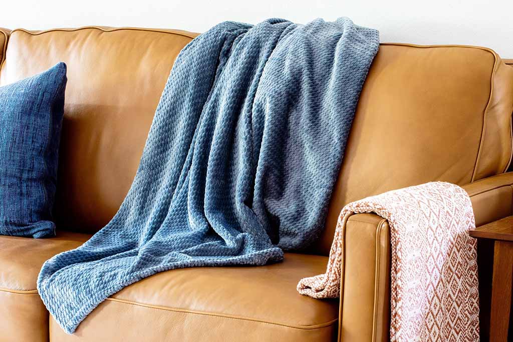 Blue textured throw blanket draped over a leather sofa, showcasing soft woven fabric with visible knit pattern and relaxed drape, ideal for modern living room décor, cozy home styling, premium throw blanket design inspiration, and private label home textile collections.