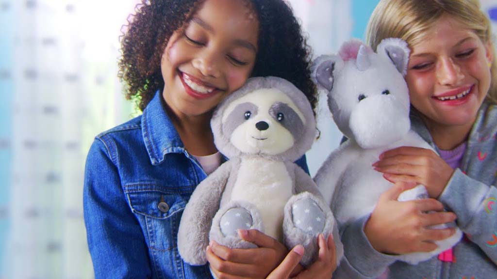 Two smiling children hugging soft plush animal toys, including a raccoon and a unicorn, showcasing gentle pastel colors, embroidered facial details, child-friendly proportions, and ultra-soft fabrics designed for comfort, emotional bonding, and safe use in children’s plush toy collections, gift retail programs, and OEM plush manufacturing.