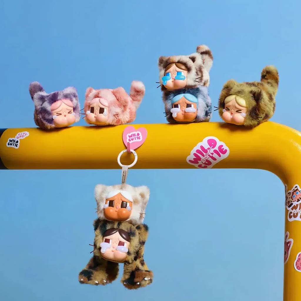 Cute Wild but Cutie Crybaby plush pendants displayed on a yellow bar, featuring various animal-pattern designs with expressive faces, including keychain versions hanging below.