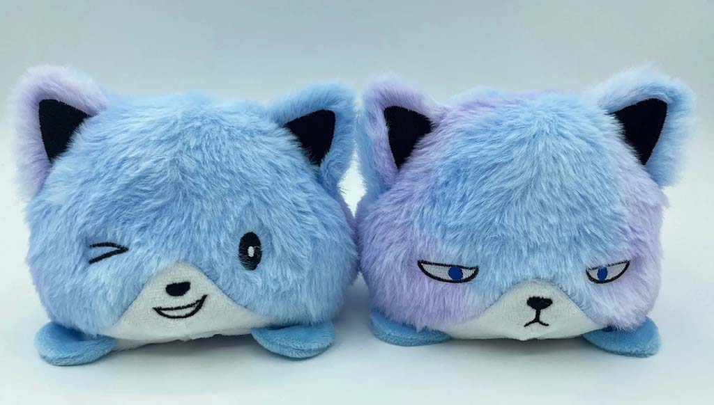 Two reversible blue fox plush toys showing different facial expressions—one happy and winking, the other serious with narrowed eyes—displayed side by side on a white background.