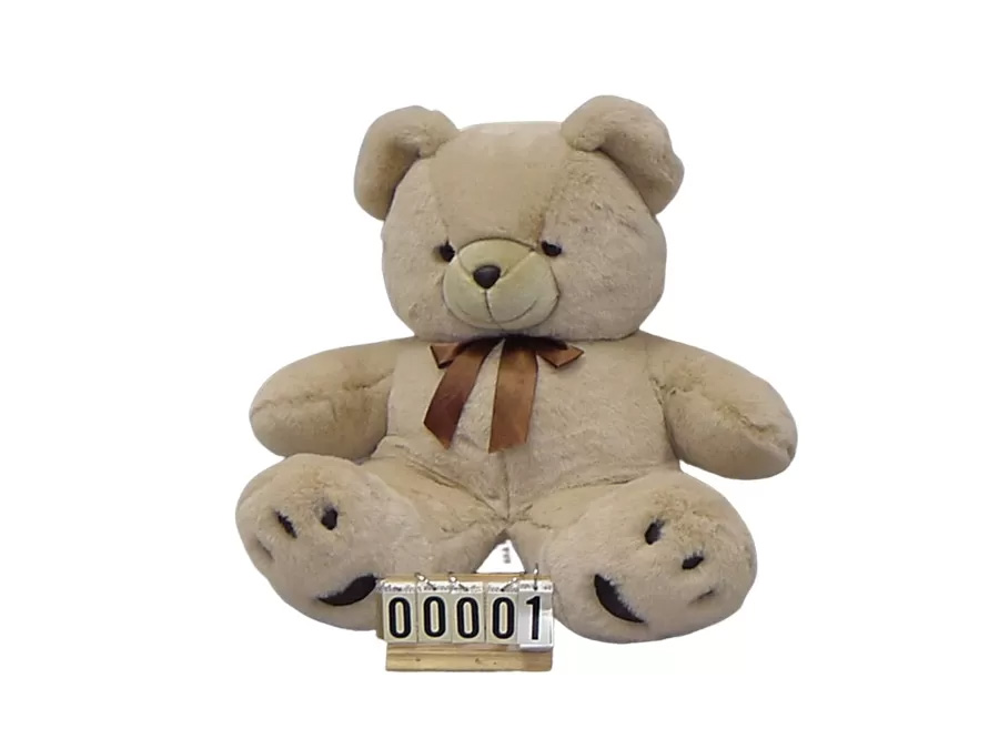 Tan teddy bear plush sitting upright with a brown ribbon bow, embroidered paw details, and a small numbered display stand in front, photographed against a white background.