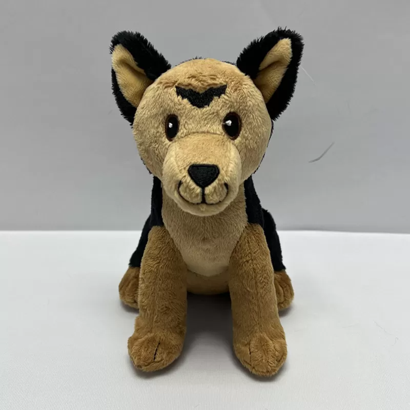 Plush toy puppy sitting upright with tan and black fur, embroidered facial details, pointed ears, and soft paws, displayed against a plain white background.