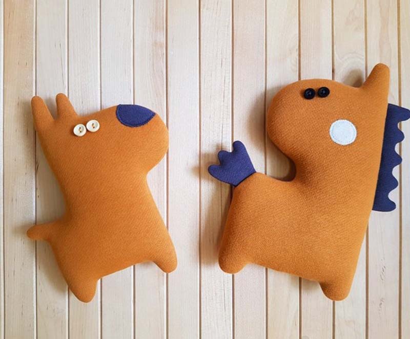 Two handmade orange plush animals displayed on a wooden background, featuring simple shapes, button eyes, and contrasting felt details in blue and white.