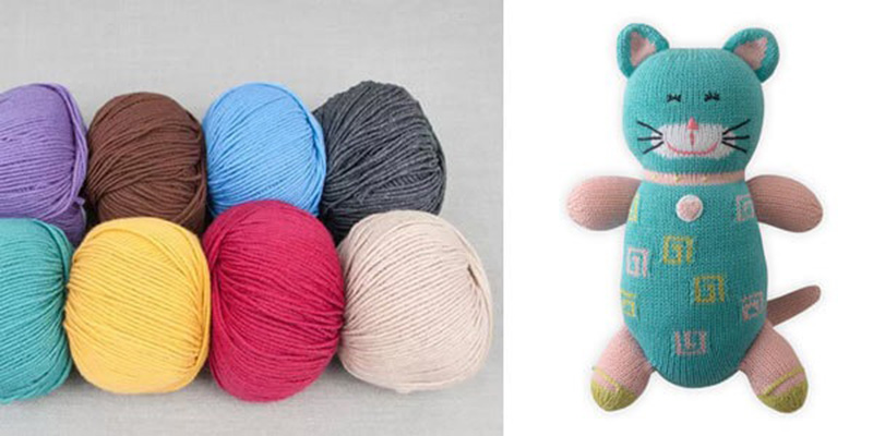 Balls of colorful cotton yarn placed beside a handmade knitted cat plush toy in teal, pink, and green.