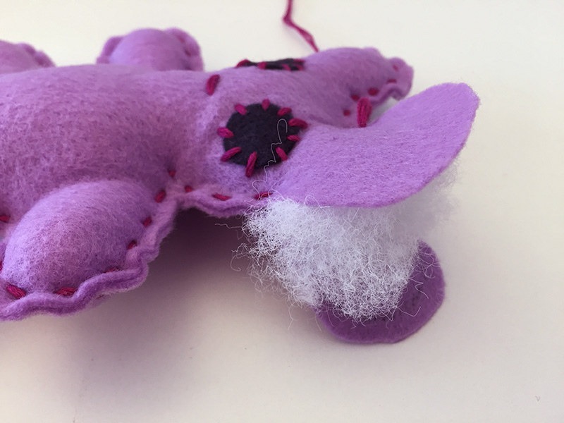 Close-up of a handmade purple felt plush toy being stuffed with white fiberfill, showing visible stitches and an open seam.