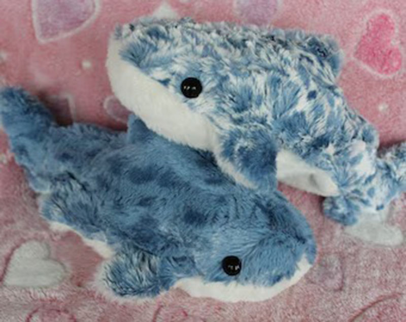 Two soft blue dolphin plush toys with spotted fabric lying on a pink blanket decorated with hearts.
