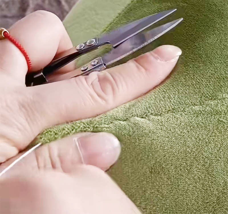 Close-up of trimming plush fabric seam using small sewing scissors.