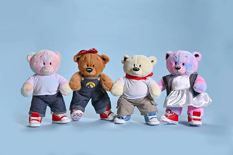 Four dressed teddy bears standing side by side, each wearing different outfits and sneakers against a blue background