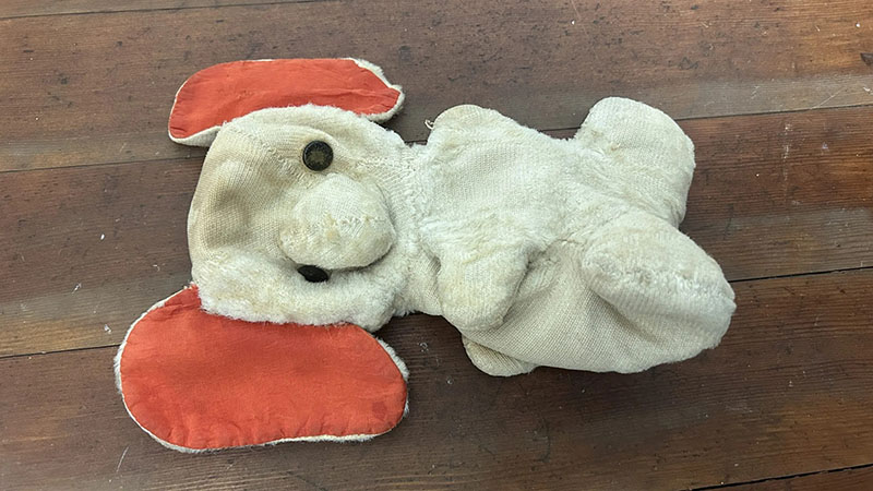 Well-worn plush toy with flattened body, faded fabric, and floppy orange ears lying on a wooden floor