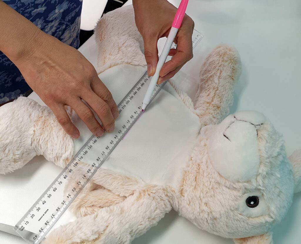Measuring plush toy dimensions using ruler and marker during quality inspection