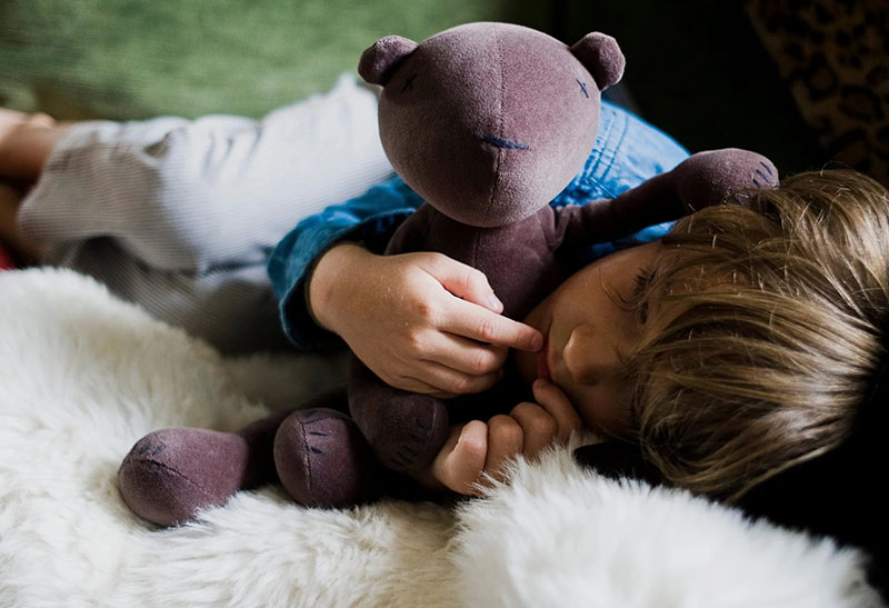 Young child resting on a soft blanket while hugging a plush teddy bear, conveying comfort and security