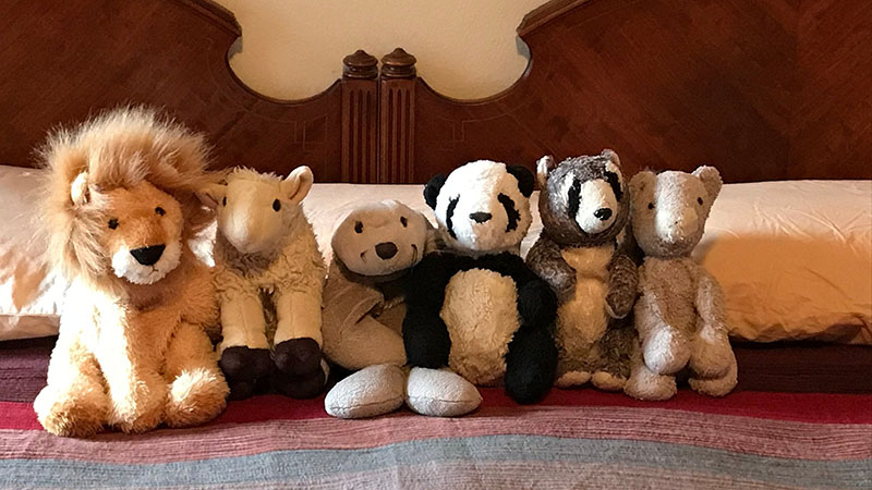 A row of plush stuffed animals, including a lion, panda, and bear, neatly lined up on a bed