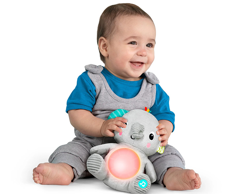 Smiling baby sitting and holding a light-up interactive plush elephant