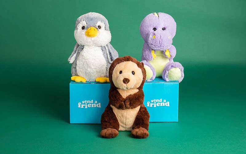 Three plush animals displayed on blue gift boxes against a green background
