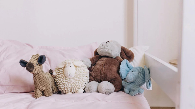 Plush and stuffed animals arranged on bed with pillows