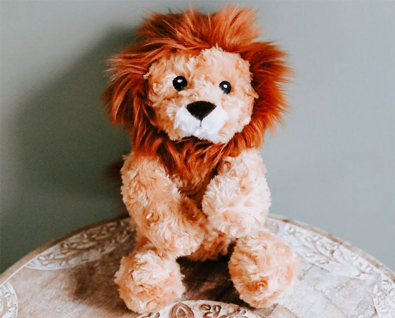 Soft plush lion with a fluffy orange mane sitting upright on a round table